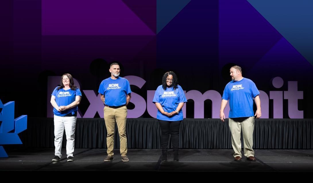 Four people in blue t-shirts standing on a stage